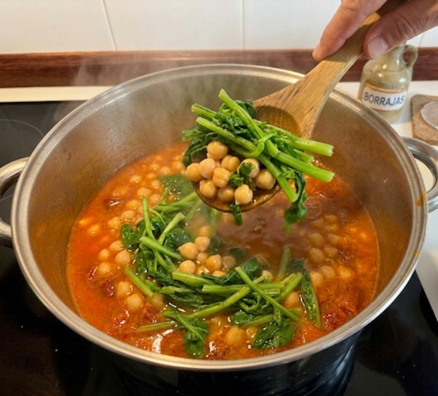 Añadiendo las borrajas a la receta de garbanzos con trozos de chistorra roja, virutas de jamón serrano y tallos de borraja