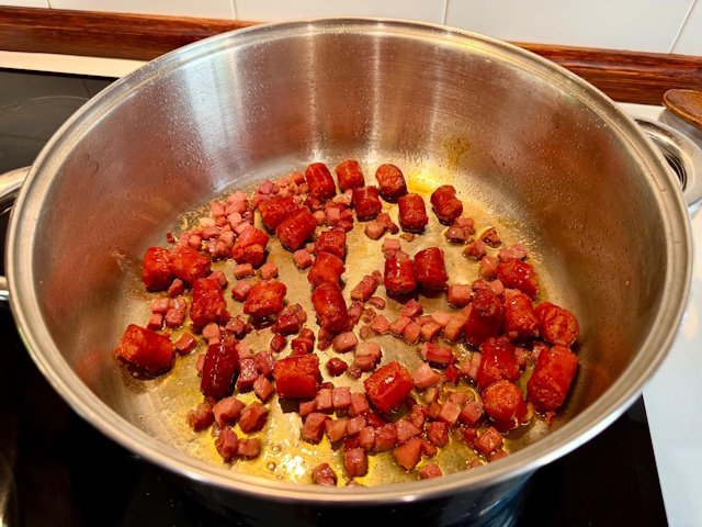 Salteado de chistorra y jamón soltando su jugo en una cazuela de cerámica para base de guiso de legumbres.